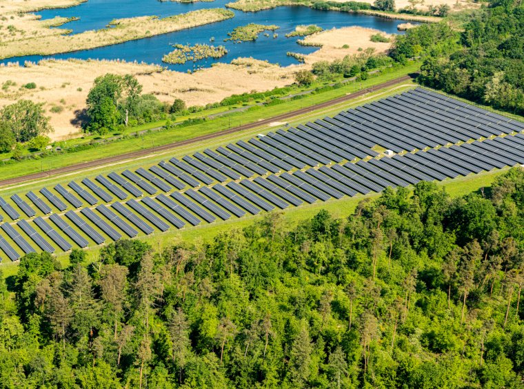 Landscape shot: solar park with railroad line behind and a lake.